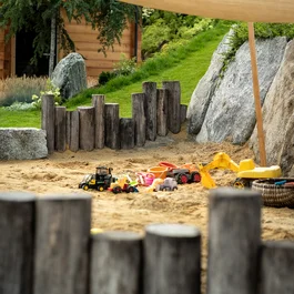 Sandkasten mit Spielzeugfahrzeugen und Holzeinfassung im Garten